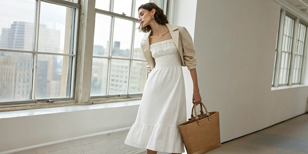 Robe smockée blanche portée avec une veste et un sac en paille pour un look élégant.